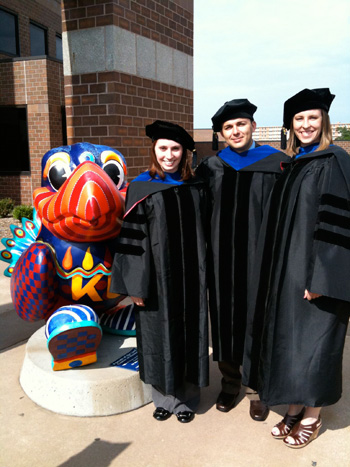 A picture of Linda Blake in her graduation gown with fellow graduates next to a Jayhawk statue.